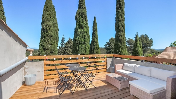 A wooden deck with a table and chairs, a sofa, and a view of tall trees. - 1 bedroom beautiful home in Verzeille (Verzeille)