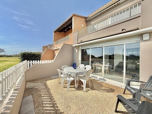A building with a patio area featuring a table and chairs, a glass door leading to an outdoor space, and a white fence. - CAP D'AGDE - Plage Richelieu / Réf 0304 (CAP D'AGDE)