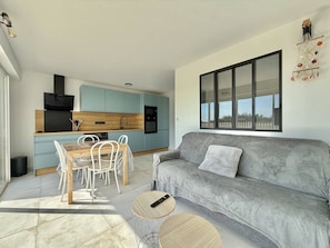 A modern kitchen with light blue cabinets, a grey sofa, and a large window. - CAP D'AGDE - Plage Richelieu / Réf 0304 (CAP D'AGDE)