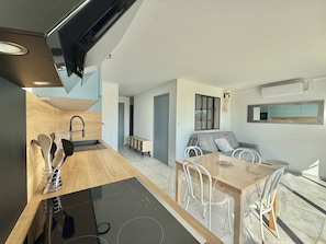 A modern kitchen with a built-in stove, a dining area with a table and chairs, and a living space with a sofa and a TV. - CAP D'AGDE - Plage Richelieu / Réf 0304 (CAP D'AGDE)