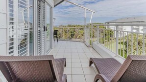 Een balkon met rieten meubels, een glazen deur en uitzicht op groen.