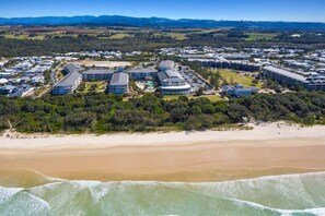 Ein Luftbild eines Küstenresorts mit mehreren Gebäuden, einem Sandstrand und freiem Blick auf den Ozean.