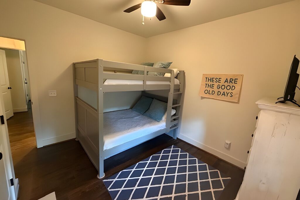 A bunk bed room with a ceiling fan, a sign on the wall, and a patterned rug.
