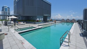 Ein Pool auf dem Dach mit einem modernen Gebäude im Hintergrund, einem klaren Himmel und Blick auf die Stadtlandschaft.