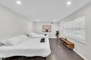 Ein modernes Hotelzimmer mit zwei Betten, einer hölzernen Bank, einer Topfpflanze und einem gerahmten Kunstwerk an der Wand.