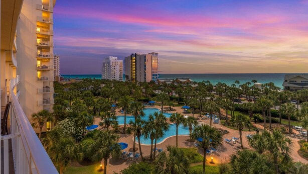Ein Resort mit Pool, Palmen und Blick auf den Ozean bei Sonnenuntergang.