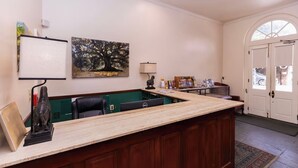 Una zona de recepción con mostrador de madera, dos sillas de oficina negras, un escritorio con ordenador, un cuadro de un árbol y una puerta con ventana.