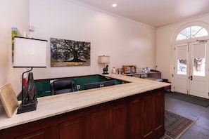 Un espace d’accueil avec un comptoir en bois, un bureau et une chaise. Il y a un tableau au mur, une lampe et une porte avec une fenêtre.