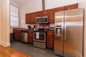 A compact kitchen with wooden cabinets, a stainless steel refrigerator, a microwave, an oven, and a coffee maker.