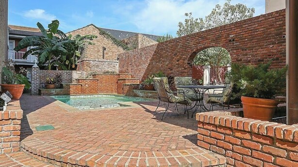 Un patio de ladrillo con piscina, mobiliario exterior y un muro de ladrillo.