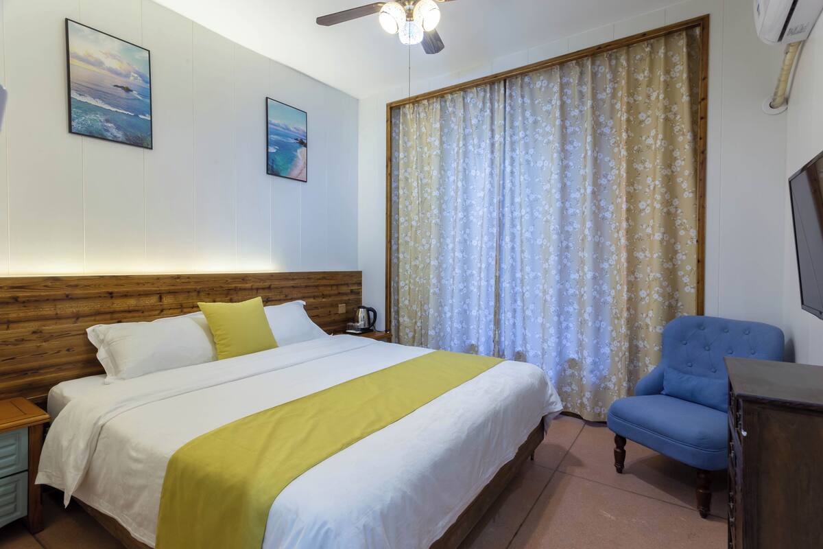 A hotel room with a bed, a chair, a television, and a window with curtains.