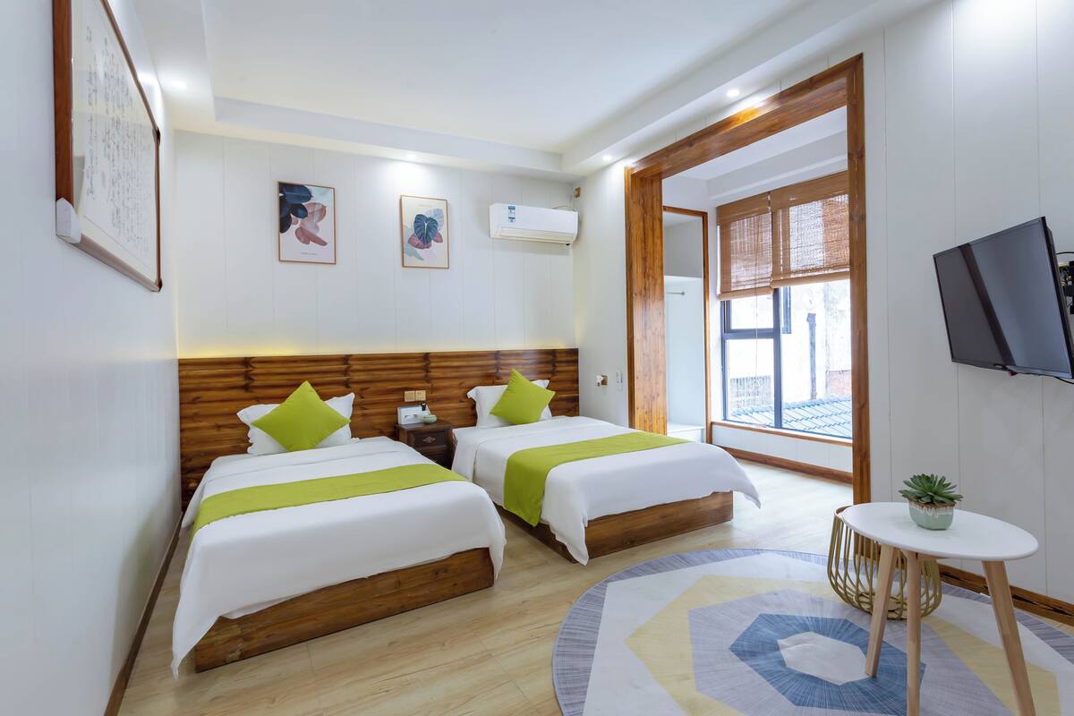A hotel room with two beds, a TV, a small table with a plant, and a window with a view.