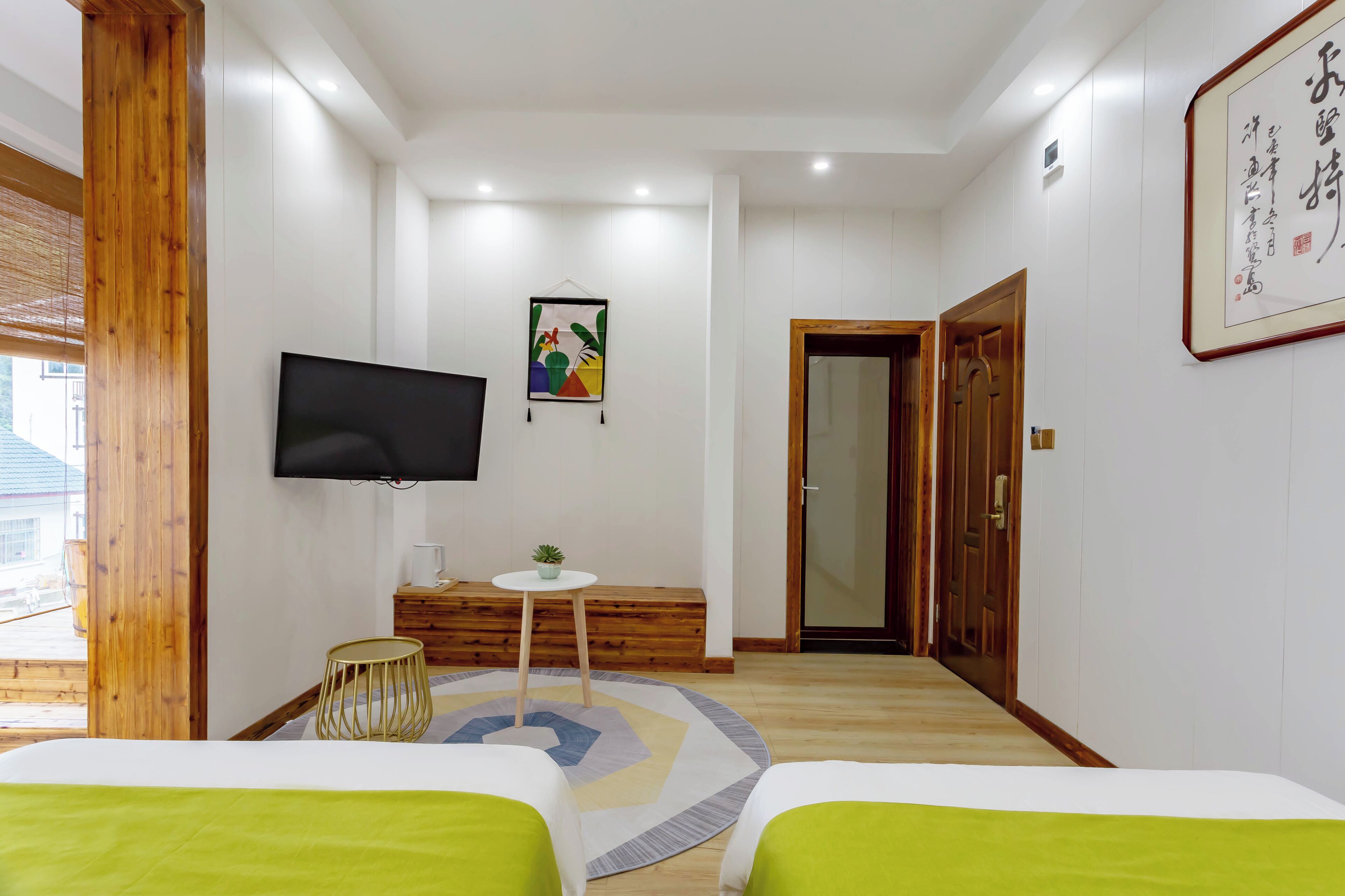 A hotel room with a bed, a TV, a small table with a plant, a wooden bench, and a framed picture on the wall.