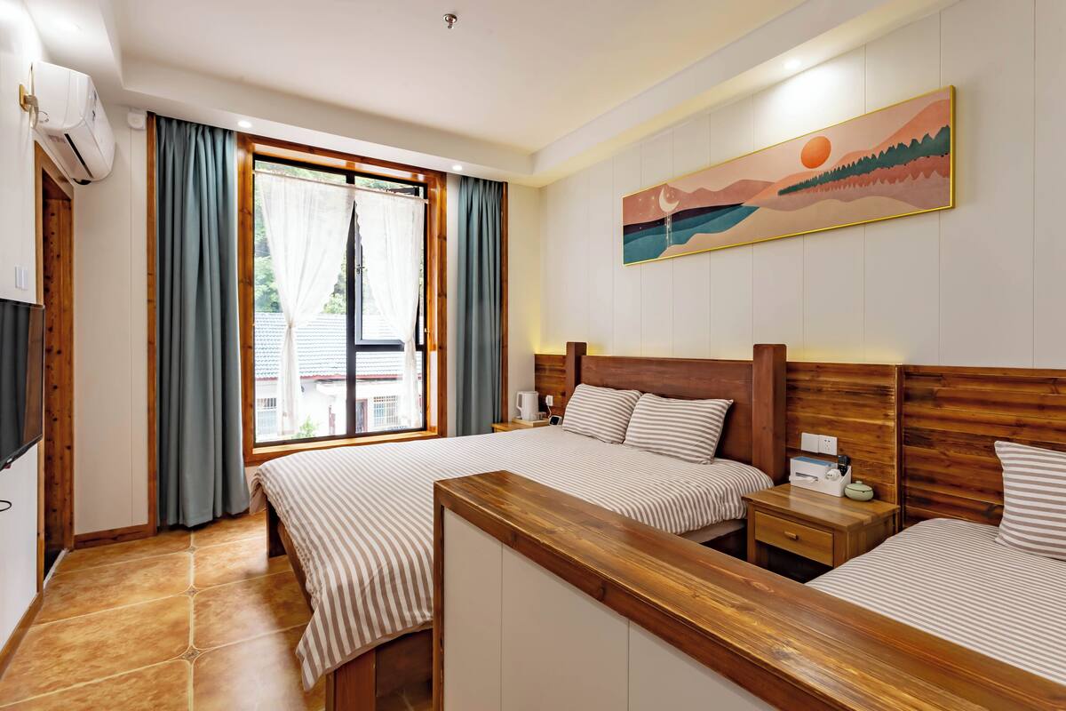 A hotel room with two beds, a wooden headboard, a window with curtains, a painting on the wall, and a tiled floor.