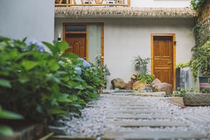 Un chemin menant à un bâtiment doté de deux portes en bois, entouré de verdure et de rochers.