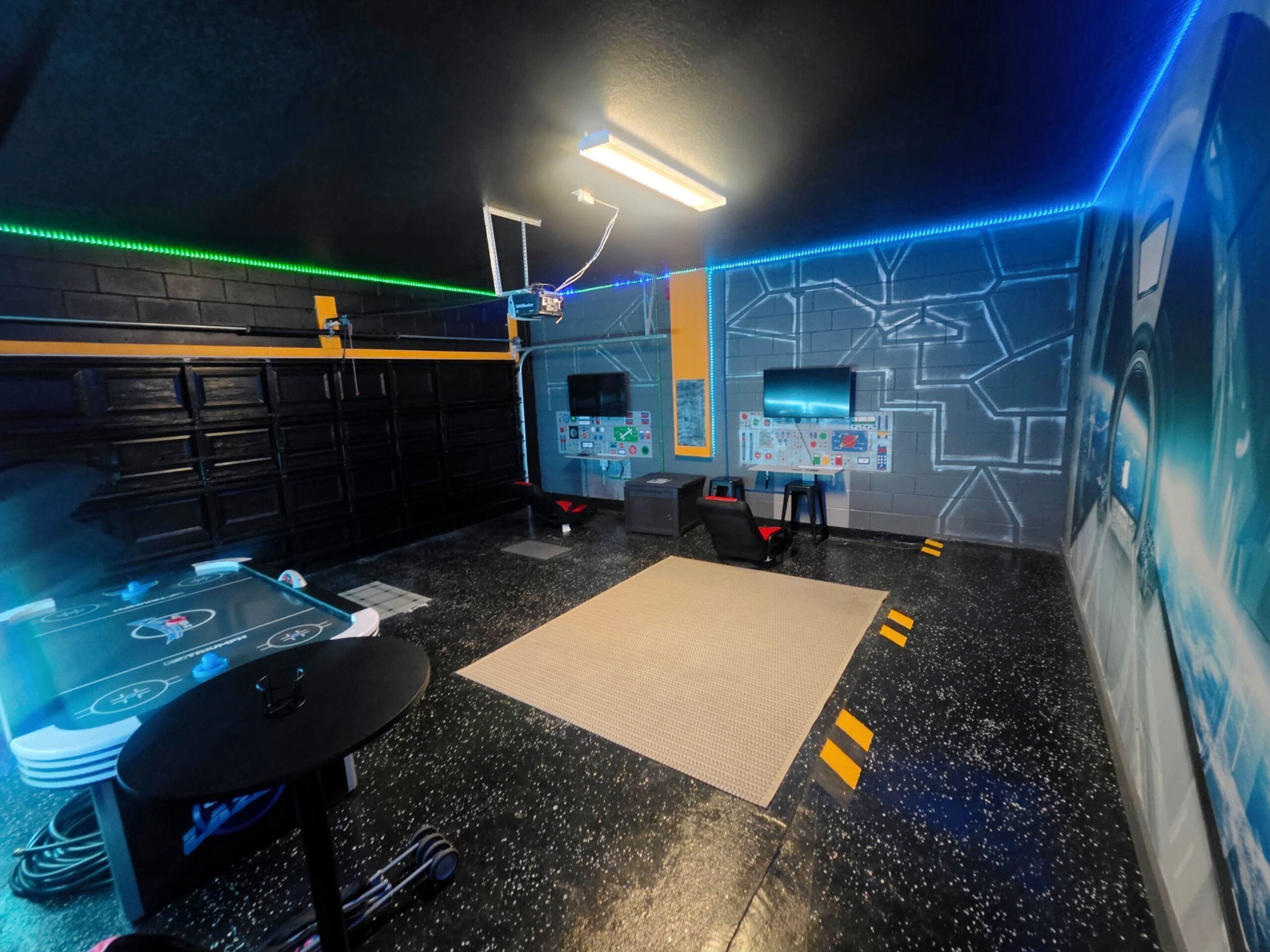 A room with a control panel, a table with a game, a chair, and a wall with a mural.