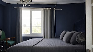Een slaapkamer met een groot bed, een raam met gordijnen, een kroonluchter en een groene fauteuil.