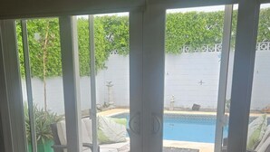 Ein Schlafzimmer mit einem großen Schiebeglasfenster, das zu einem Außenbereich mit Pool und Liegestühlen führt.