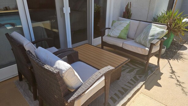 Eine Terrasse mit Korbmöbeln, eine Glastür zu einem Pool und ein Blumentopf.