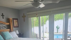 Ein Schlafzimmer mit einem Bett, einem Deckenventilator, einem großen Fenster und Blick auf einen Pool.