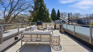 A rooftop terrace with a sofa, a small table, and a decorative stool. - Luxury Dunbar Home — Rooftop, Putting Green & Park (Vancouver)