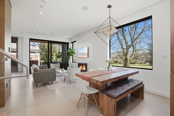 A modern living room with a wooden dining table, white sofas, and a fireplace. - Luxury Dunbar Home — Rooftop, Putting Green & Park (Vancouver)