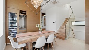 A modern kitchen with a wooden table, white chairs, a hanging light fixture, and a built-in wine rack. - Luxury Dunbar Home — Rooftop, Putting Green & Park (Vancouver)