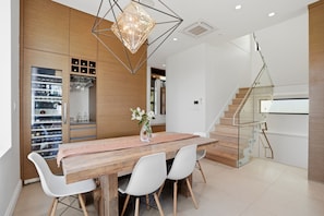 A modern kitchen with a wooden table, white chairs, a hanging light fixture, and a built-in wine rack. - Luxury Dunbar Home — Rooftop, Putting Green & Park (Vancouver)