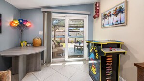 A room with a seating area, a table with balloons, a game machine, and a painting of palm trees. - Family 3BR w/ Pool | Game Room I Walk to WaterPark (Margate)