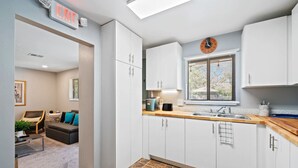 A modern kitchen with white cabinets, a stone tile floor, a wooden countertop, and a clock on the wall.