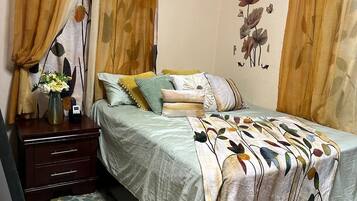 Un dormitorio con cama, mesita de noche, aire acondicionado y decoración floral en la pared.