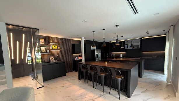 Una cucina moderna con isola centrale, sgabelli da bar, illuminazione a sospensione e pavimento in marmo.