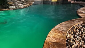 Una piscina con acqua cristallina, circondata da una terrazza in pietra e palme.