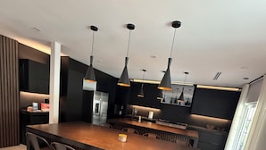 Una cucina moderna con isola centrale, sgabelli da bar, illuminazione a sospensione e pavimento in marmo.