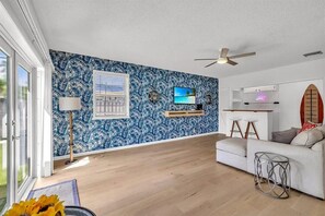 A modern living room with a blue patterned wall, a ceiling fan, a TV, and a white sofa.