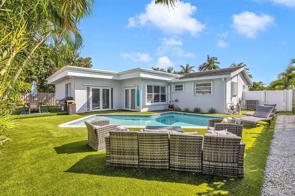 A modern house with a swimming pool, outdoor furniture, and a well-maintained lawn.