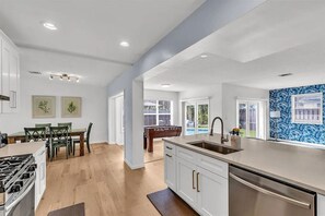 A modern kitchen with a central island, a dining area with a table and chairs, and a view of the outdoors.