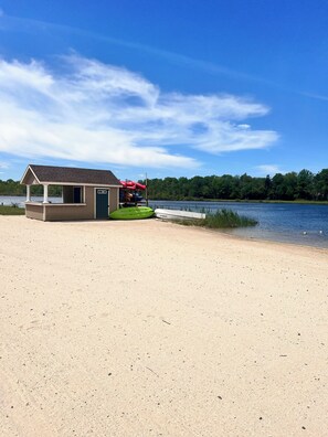 A beachside structure with a small building, kayaks, and a dock extending into a lake. - Peaceful Poconos Escape! Fireplace + Firepit + Lake & Pool Access. (Tobyhanna)
