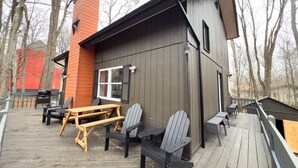 Un terrazzo in legno con poltrone Adirondack, un tavolo da picnic e un piccolo edificio con una finestra e una porta.