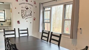Un'area pranzo con un tavolo lungo e sei sedie, una finestra con tende e un adesivo murale con scritte a tema caffè.