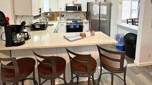 Una cucina moderna con mobili bianchi, un'isola centrale con sgabelli da bar e un cartello con scritto 'Benvenuti dal lato soleggiato'.