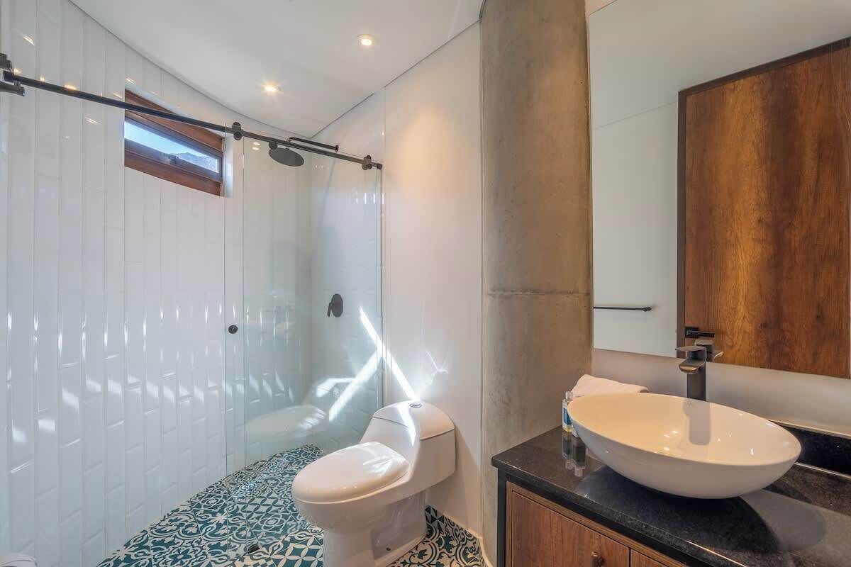 A modern bathroom with a glass-enclosed shower, a white toilet, and a large vessel sink.