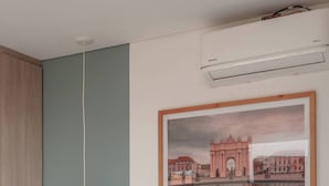 Un llit ben fet amb llençols blancs, una làmpada penjant i una fotografia encadrada d'un paisatge urbà a la paret.