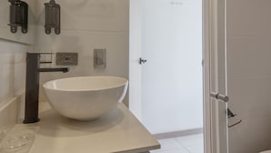 Un bany modern amb un gran lavabo blanc, un penjador de fusta, una cabina de dutxa de vidre i un vàter.