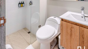 A modern bathroom with a glass-enclosed shower, a white toilet, a wooden vanity with a mirror, and a white sink. - NOK Modern Studio in Chapinero (Bogotá)