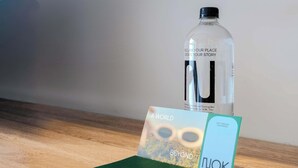 A clear plastic water bottle, a green booklet with 'NOK' printed on it, a card with 'A WORLD BEYOND' and 'NUOK' on it, and a black pen on a wooden surface. - NOK Modern Studio in Chapinero (Bogotá)