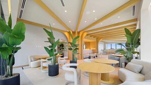 Un interior moderno con una zona de estar central, plantas en macetas grandes y vistas de la ciudad.