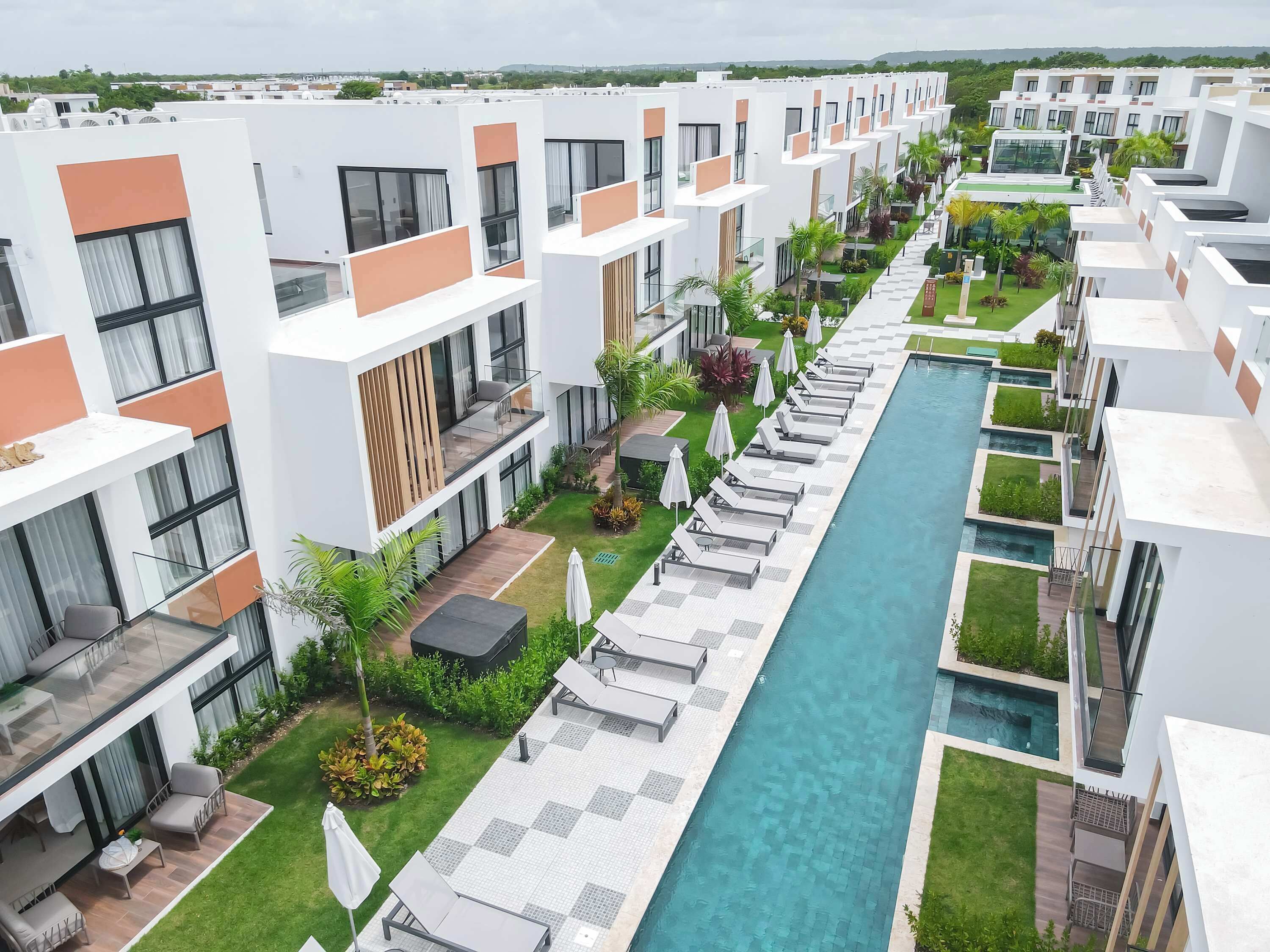 Un hotel moderno con piscina central, varios balcones y exuberante jardinería.