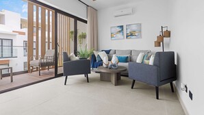 Ein modernes Wohnzimmer mit einer Couch, zwei Sesseln, einem Couchtisch und einem Deckenventilator. Ein großes Fenster bietet Blick auf Gebäude außerhalb.