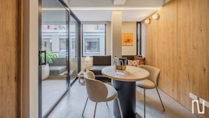 A modern room with a round table, two chairs, a sofa, and a glass partition. - NOK Designer Apartment 1BR in Zona Rosa (Bogotá)